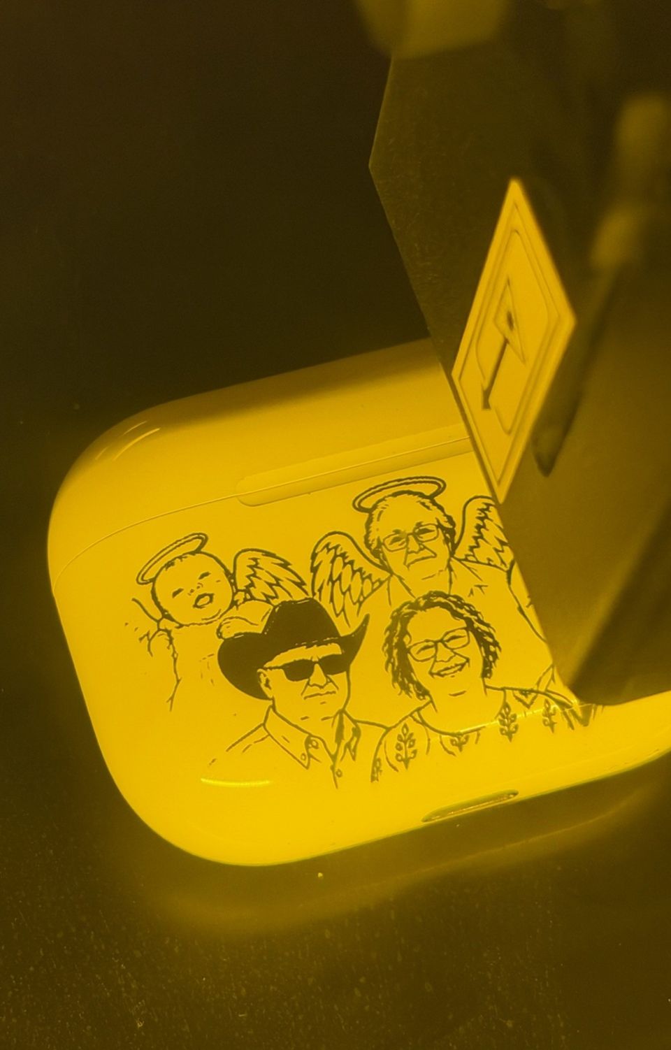 An earbud case under a laser head, with a line-art portrait being engraved.