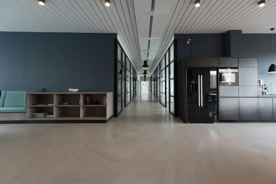 A modern office interior with a lounge, glass-walled rooms, and a long corridor. No people.